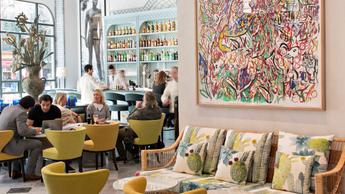 Stylish cafe interior with patrons seated, vibrant abstract art on the wall, and a well-stocked bar in the background.