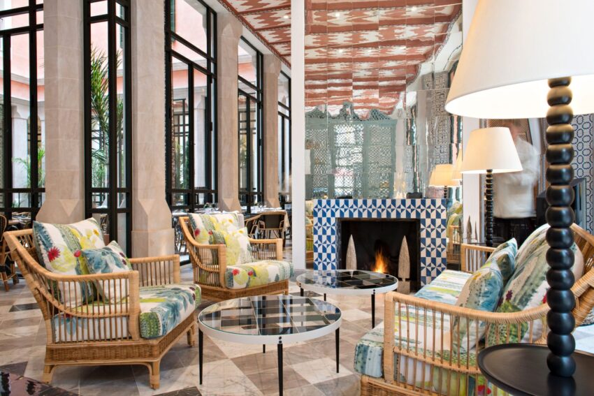 Stylish hotel lobby with wicker chairs, patterned cushions, glass tables, and a tiled fireplace.