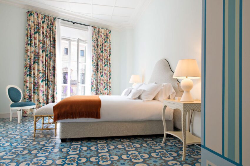 Modern bedroom with patterned floor, floral curtains, white bedding, and soft lighting from table lamps.