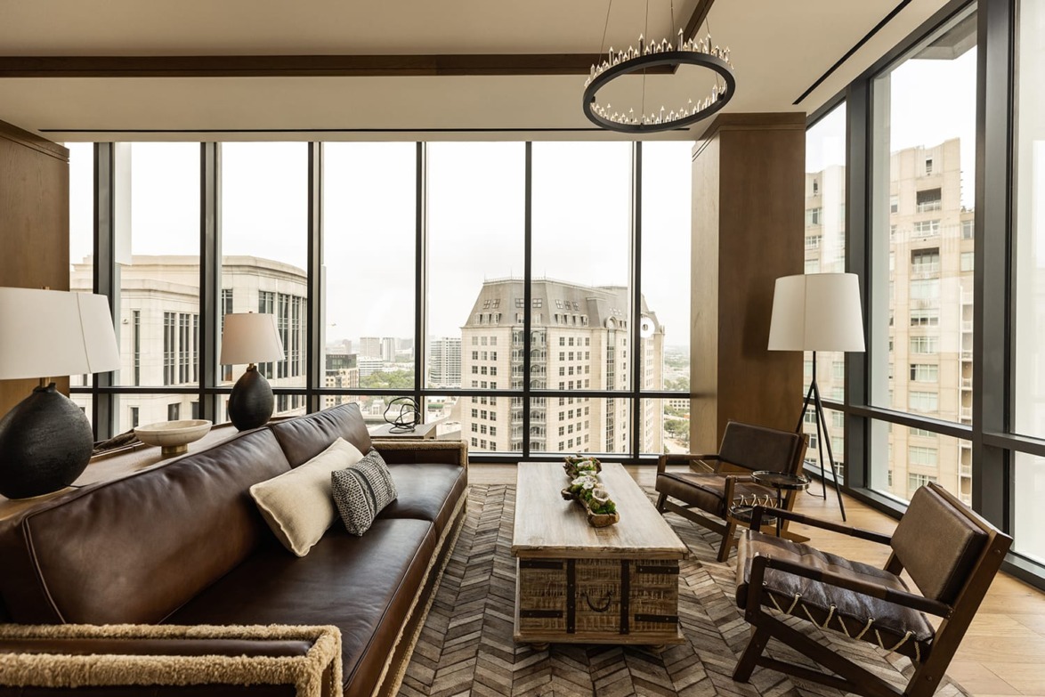 Luxurious modern living room with leather sofa, large windows offering a city view, a wooden table, and stylish decor.