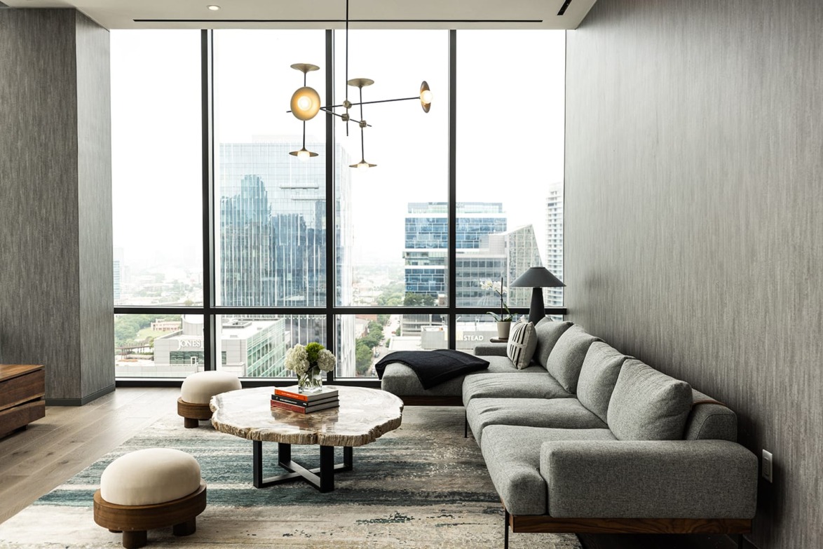Modern living room with large windows, gray sofa, round coffee table, and cityscape view.