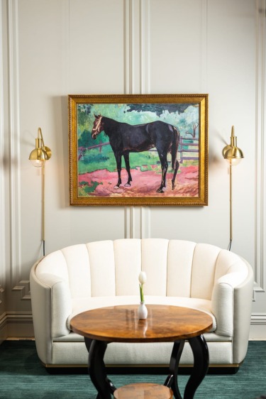 Elegant room with a white sofa, round wooden table, and a framed painting of a horse on the wall.