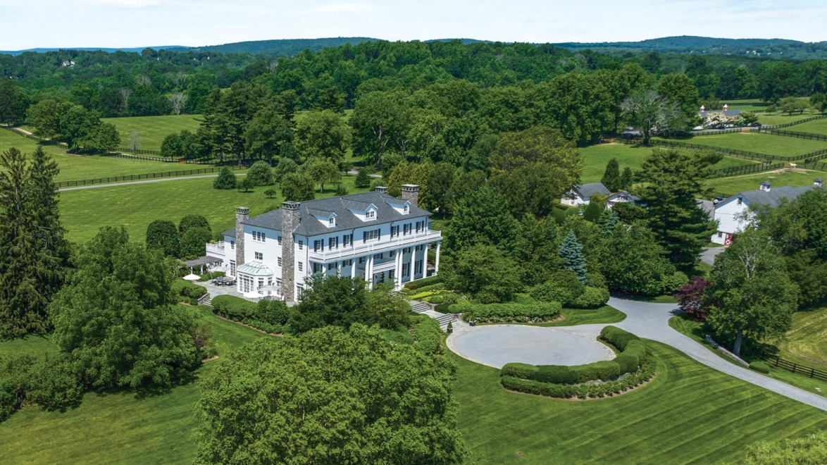 Aerial view of a large white mansion surrounded by lush green lawns and trees.