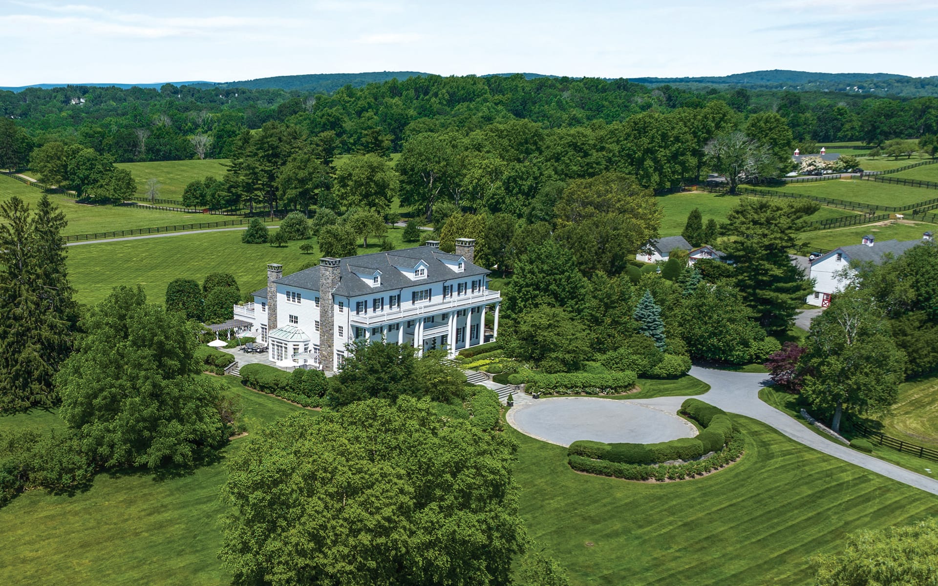 Aerial view of a large white mansion surrounded by lush green lawns and trees.