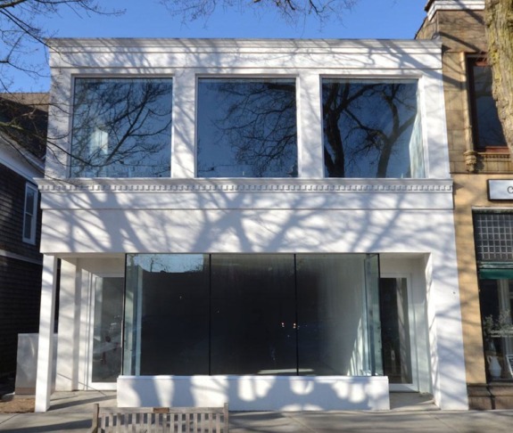 white two-story building with large glass windows and tree shadows on the wall