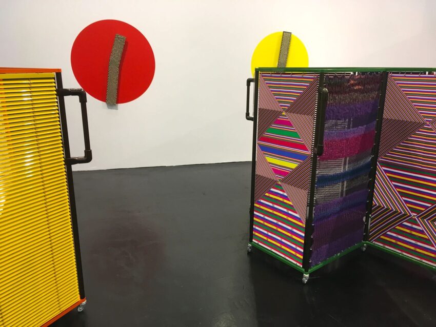 Colorful geometric art installations with striped patterns, circular shapes, and textured elements displayed in a gallery setting.