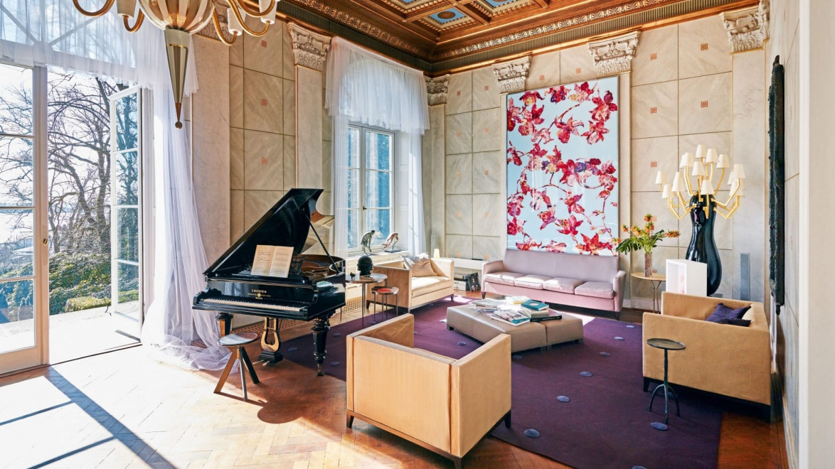 Elegant living room with grand piano, modern furniture, large windows, and a vibrant floral art piece on the wall.