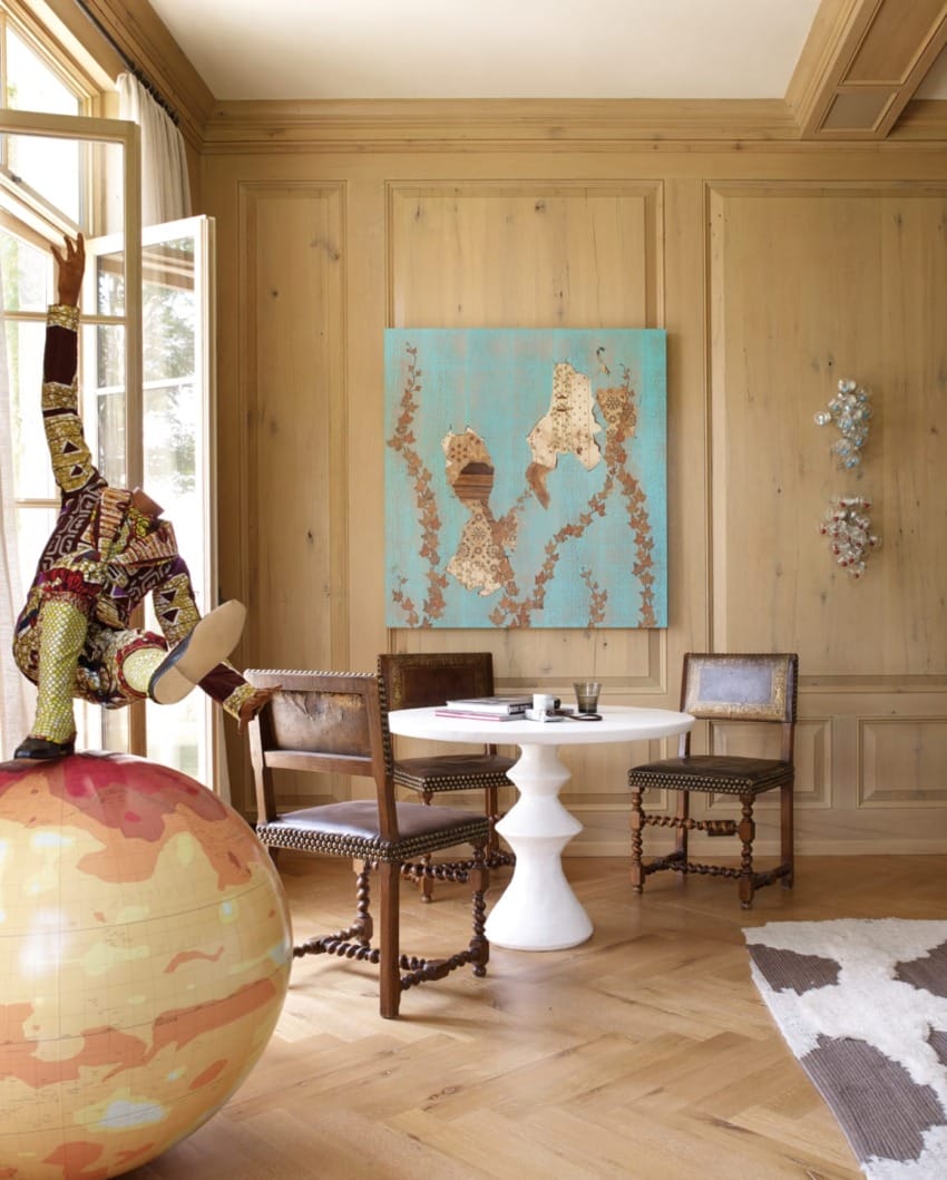 Room with modern art, globe sculpture, wooden chairs, small round table, and large painting on wood-paneled wall.