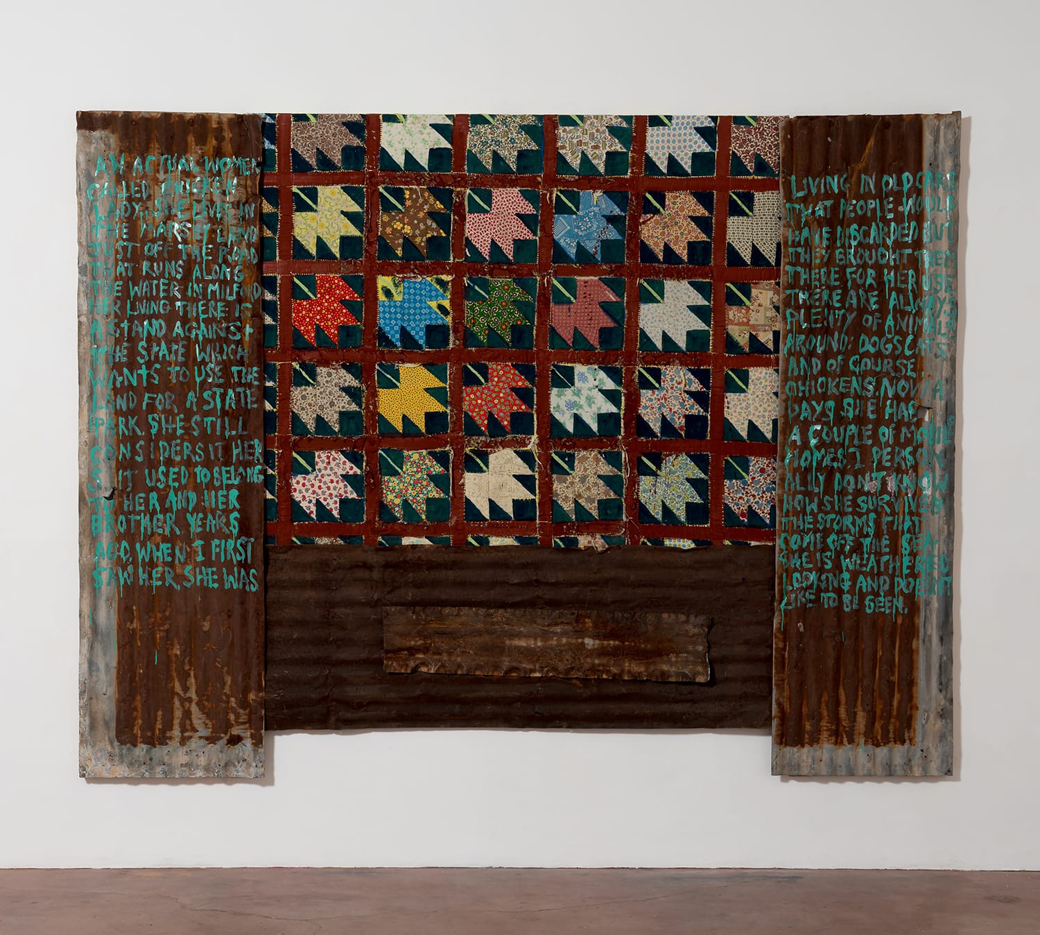 Patchwork quilt with colorful patterns on a corrugated metal background, featuring handwritten text on both sides.