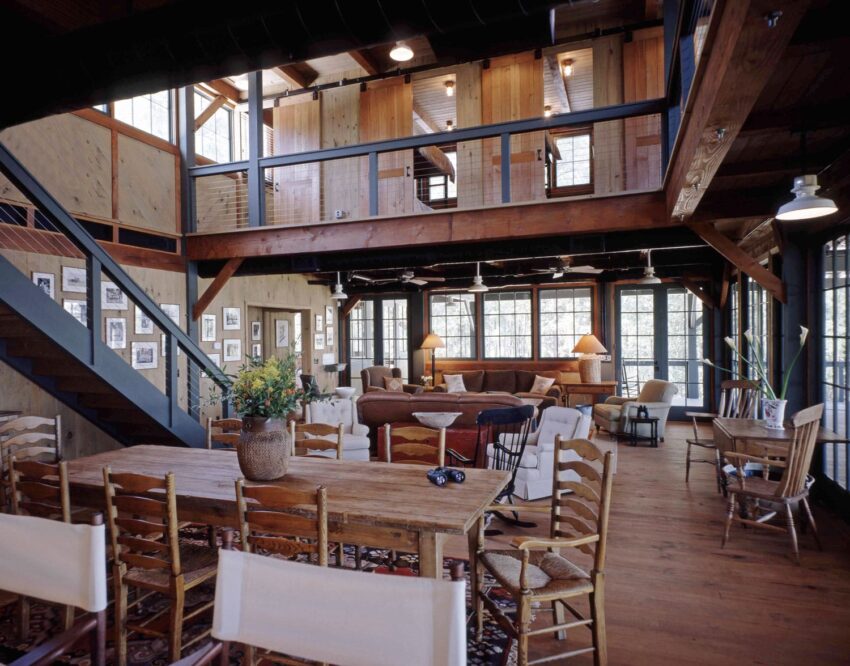 Rustic living room with wooden beams, large dining table, cozy seating area, and upstairs loft.