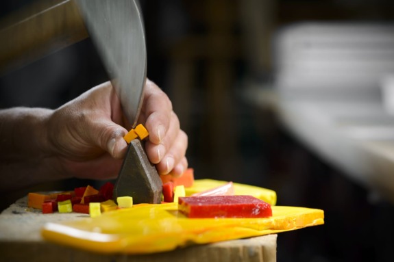 Person cutting colorful candy pieces on a table with a large knife in a candy shop.