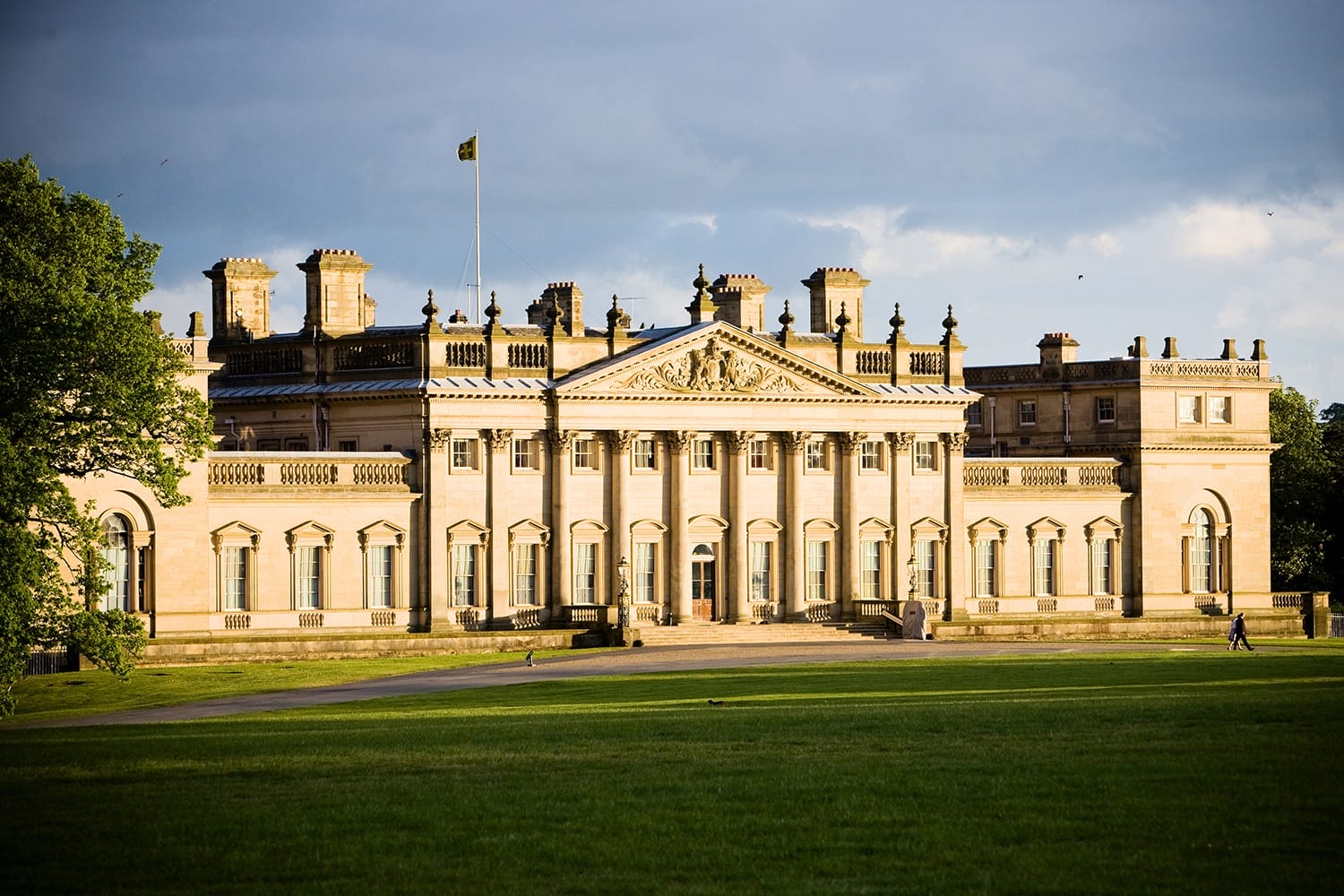 Stately home with neoclassical architecture, large columns, and manicured green lawn under a partly cloudy sky.