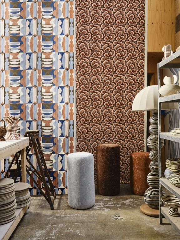 Ceramic studio with colorful patterned wallpaper, round stools, and shelves filled with pottery pieces.