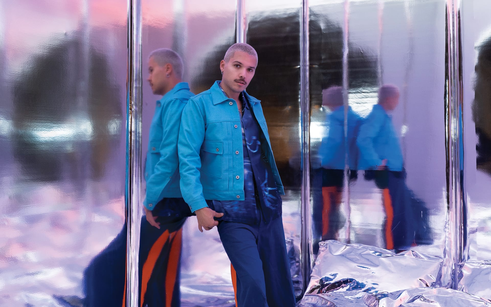 Man in a blue jacket standing in a reflective room with mirrored walls and shiny surfaces.