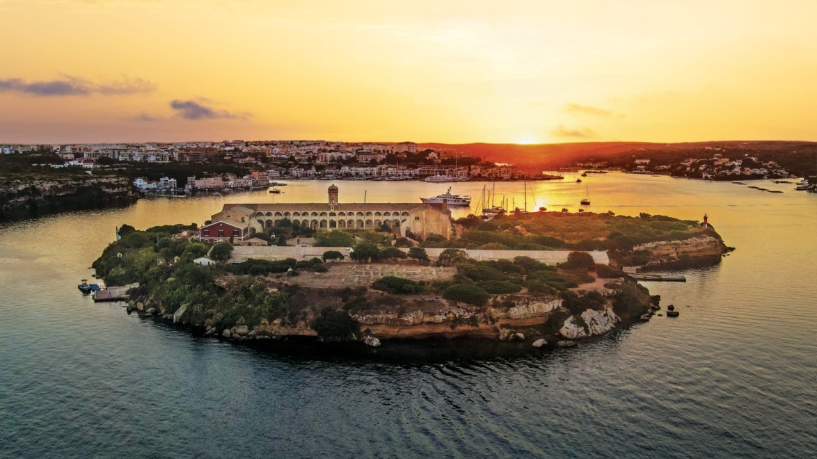 Aerial view of an island with ancient fortress surrounded by water, during a golden sunset.