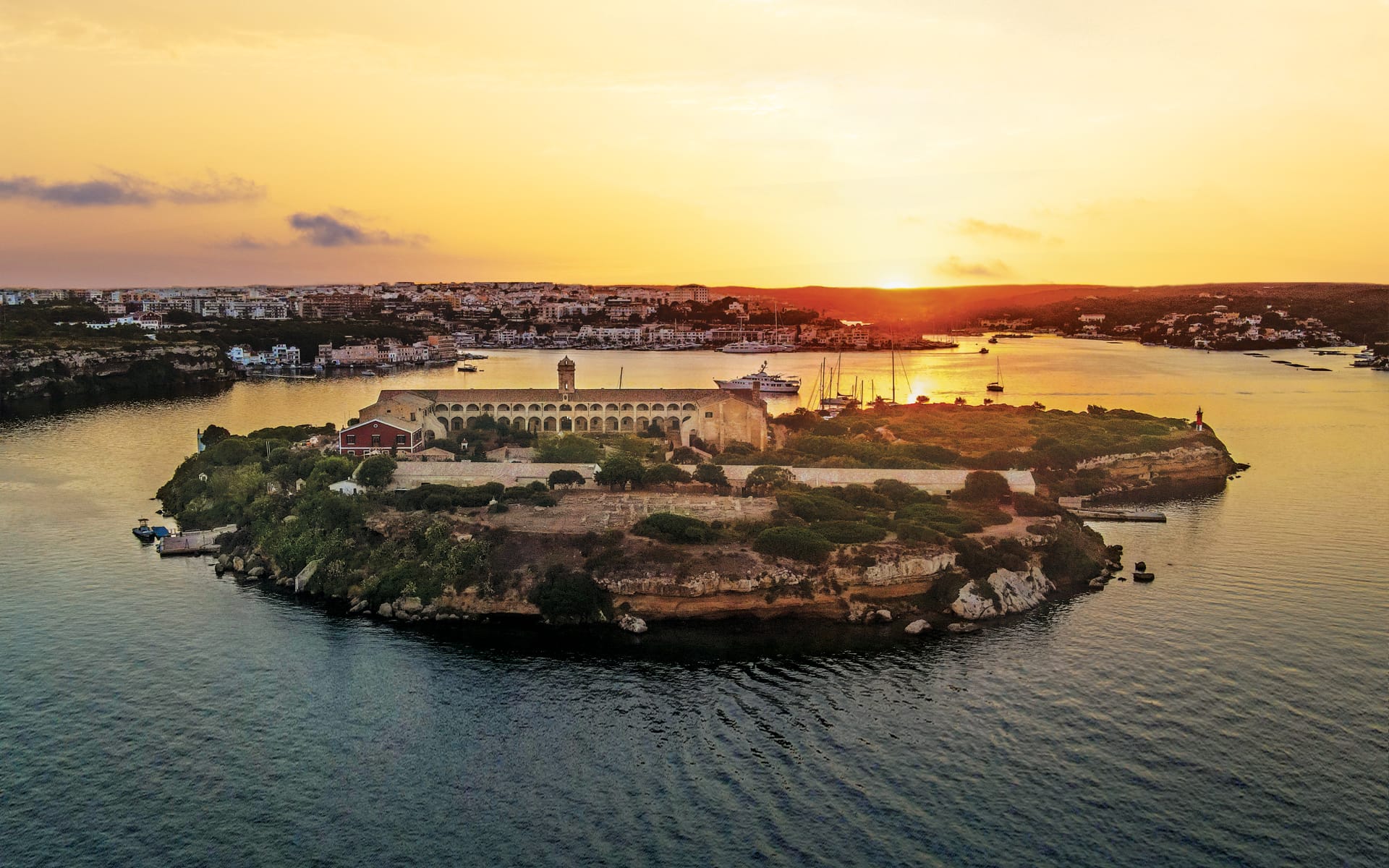 Aerial view of an island with ancient fortress surrounded by water, during a golden sunset.
