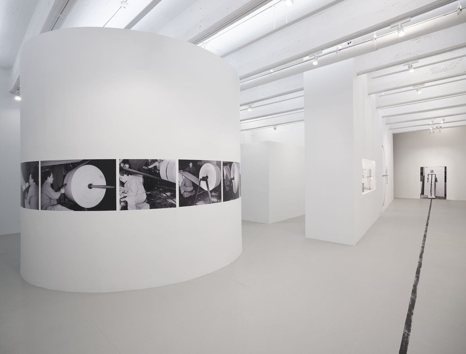 Modern art gallery interior with white walls, black-and-white photographs displayed on rounded and flat surfaces.