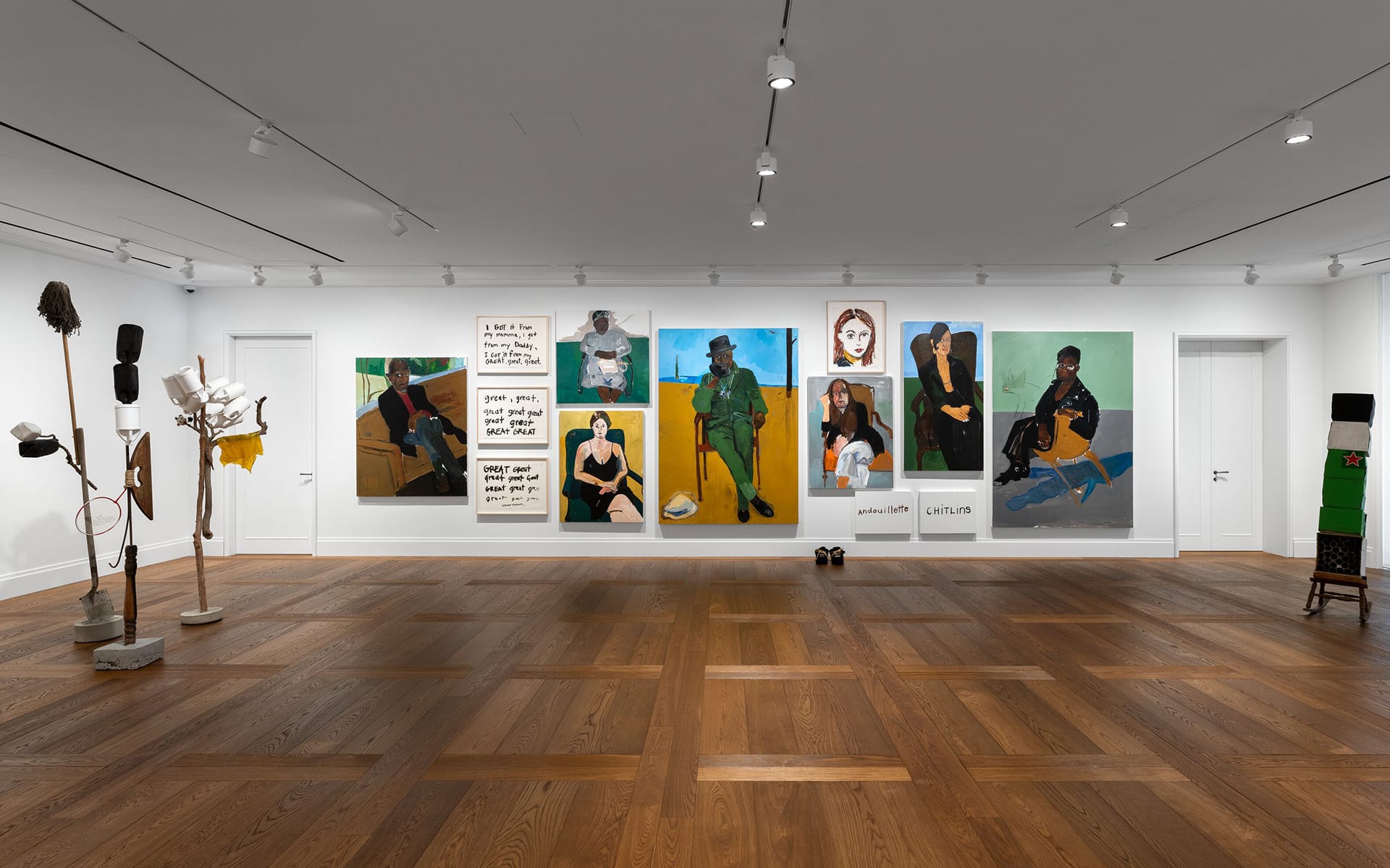 Art gallery with various colorful portraits on the wall and sculptural installations on wooden floor in a well-lit room.