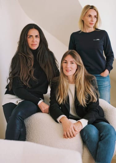 Three women posing in a casual setting with a neutral background, dressed in comfortable and stylish outfits.