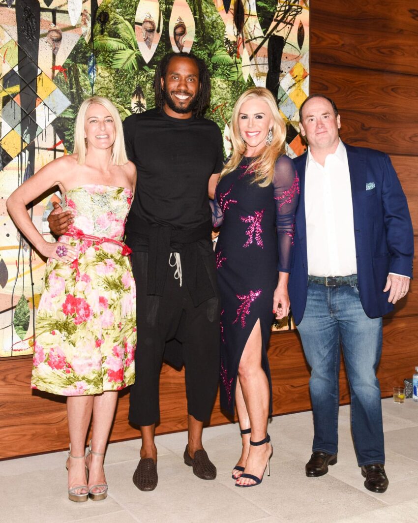 Group of four people standing together, two women and two men, smiling in front of a colorful abstract painting.