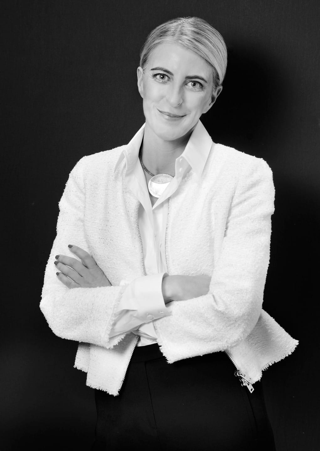 Person in professional attire with arms crossed, smiling confidently against a dark background, black and white photograph.