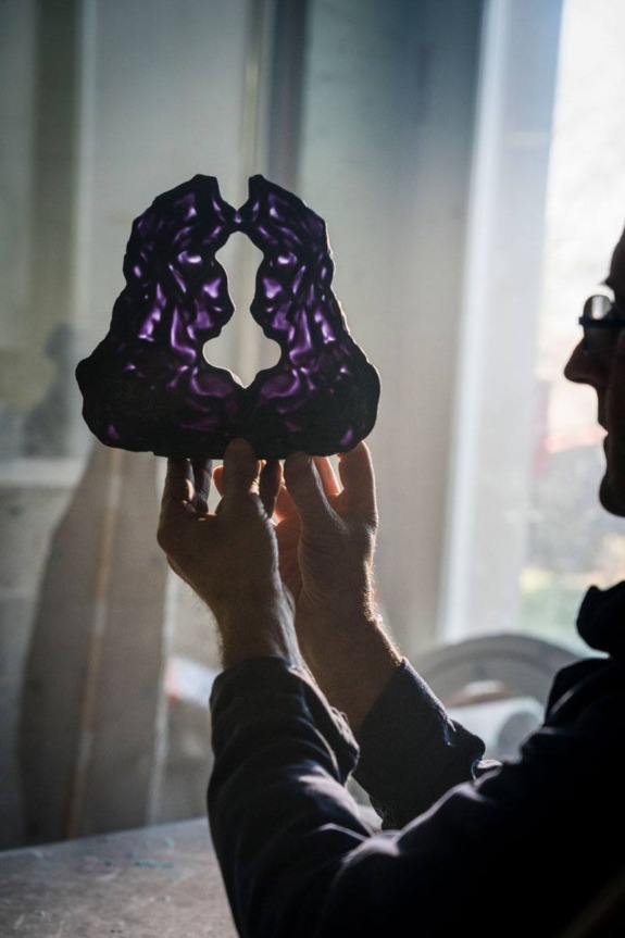 Person holding a purple translucent sculpture with two facing silhouettes by a window.
