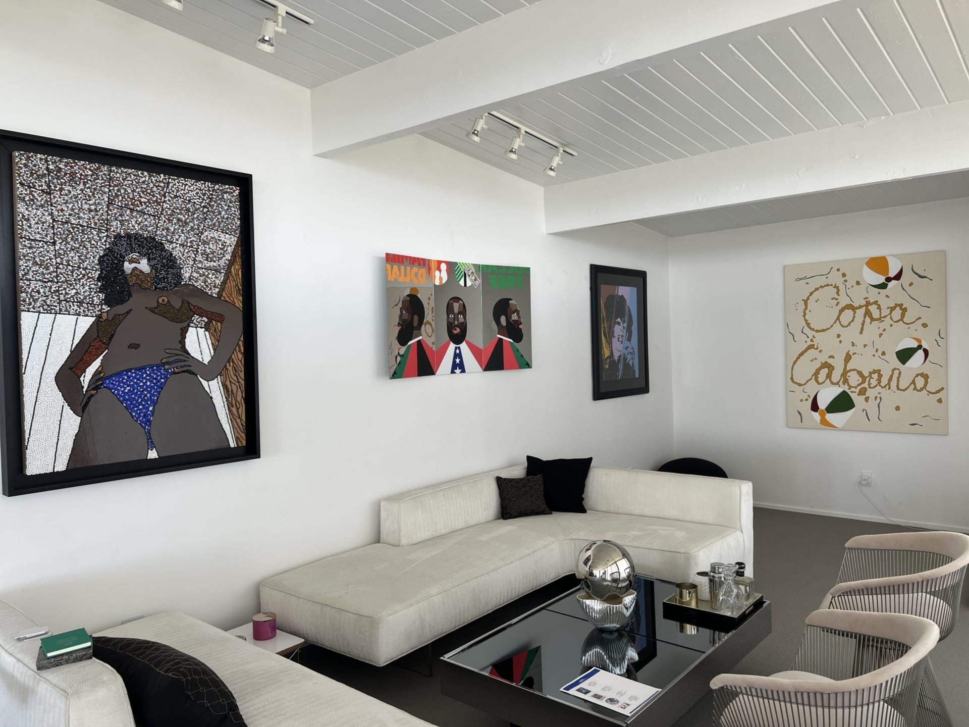 modern art pieces hanging on white walls in a contemporary living room with white sofas and a reflective coffee table