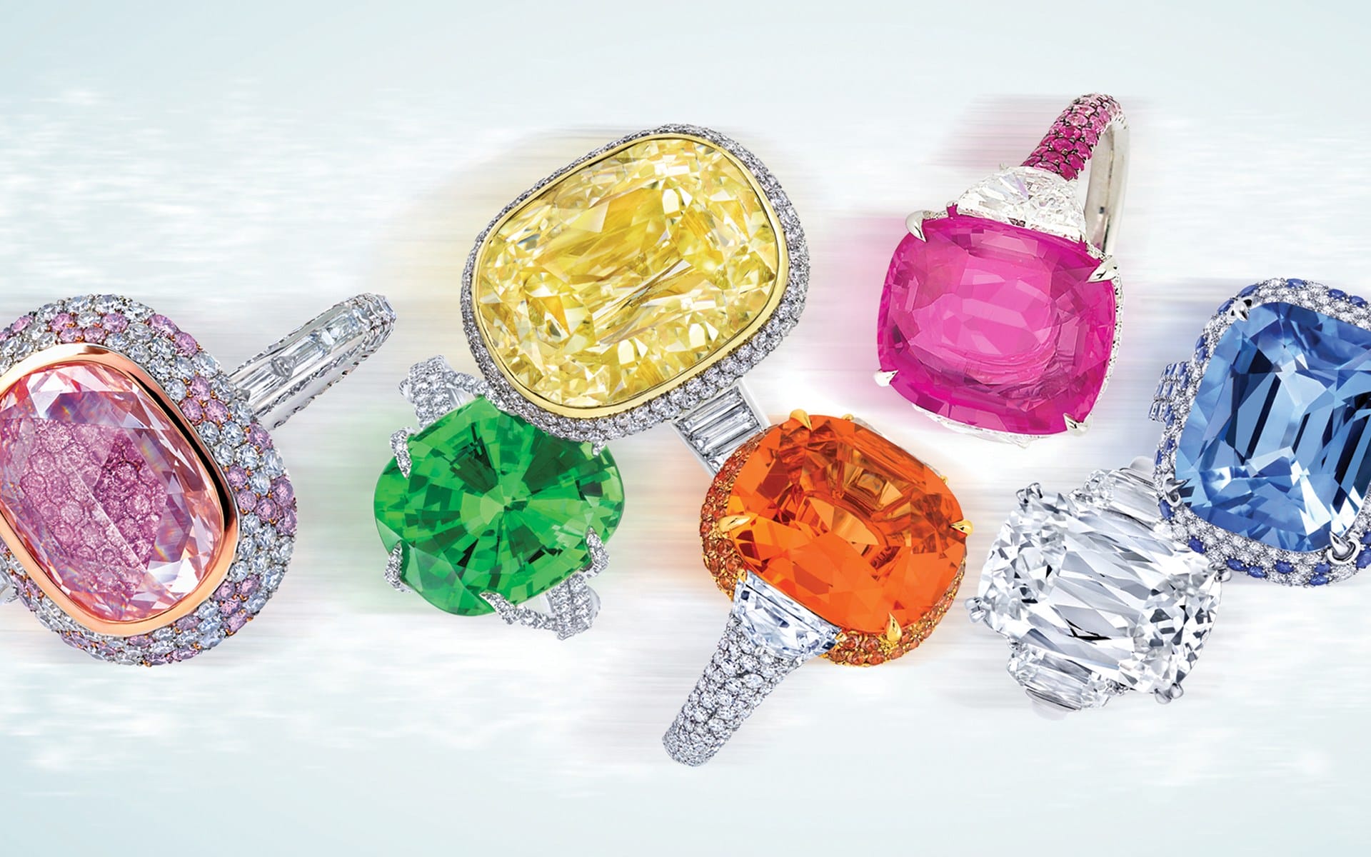 Assorted colorful gemstone rings with diamonds arranged on a light background.