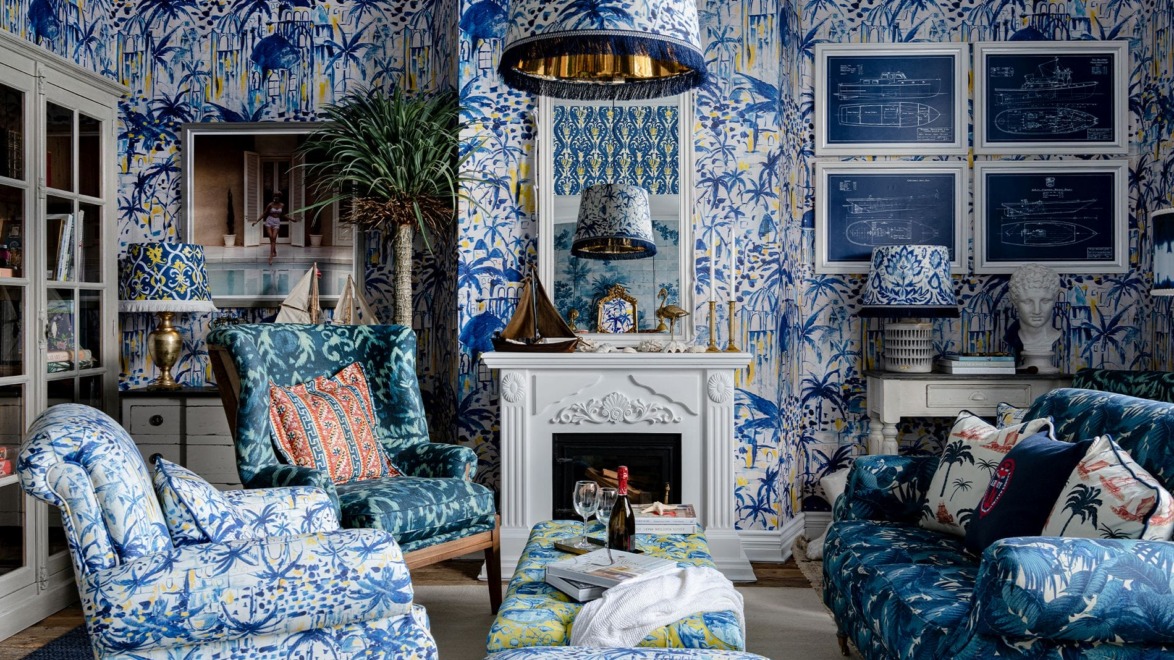 Colorful living room with blue tropical-themed wallpaper, vibrant furniture, and nautical decor elements, centered around a fireplace.