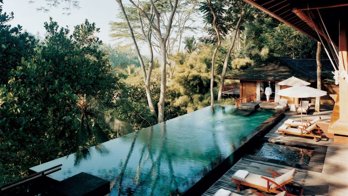 Luxurious outdoor infinity pool overlooking lush greenery surrounded by lounge chairs and umbrellas at a tropical resort.