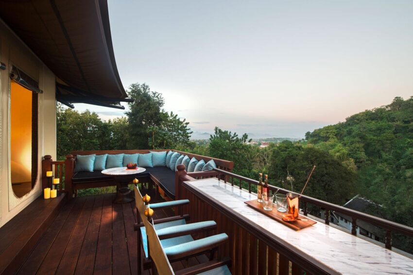 Luxury outdoor terrace with seating area, marble table, candles, and forest view at sunset.