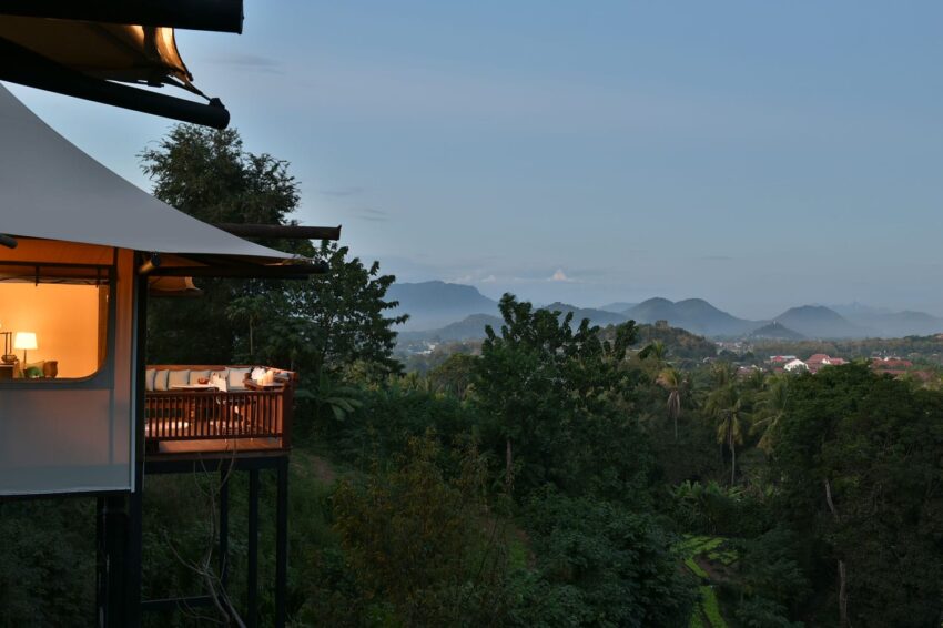 Luxury tented villa overlooking lush green landscape with distant mountains at dusk.