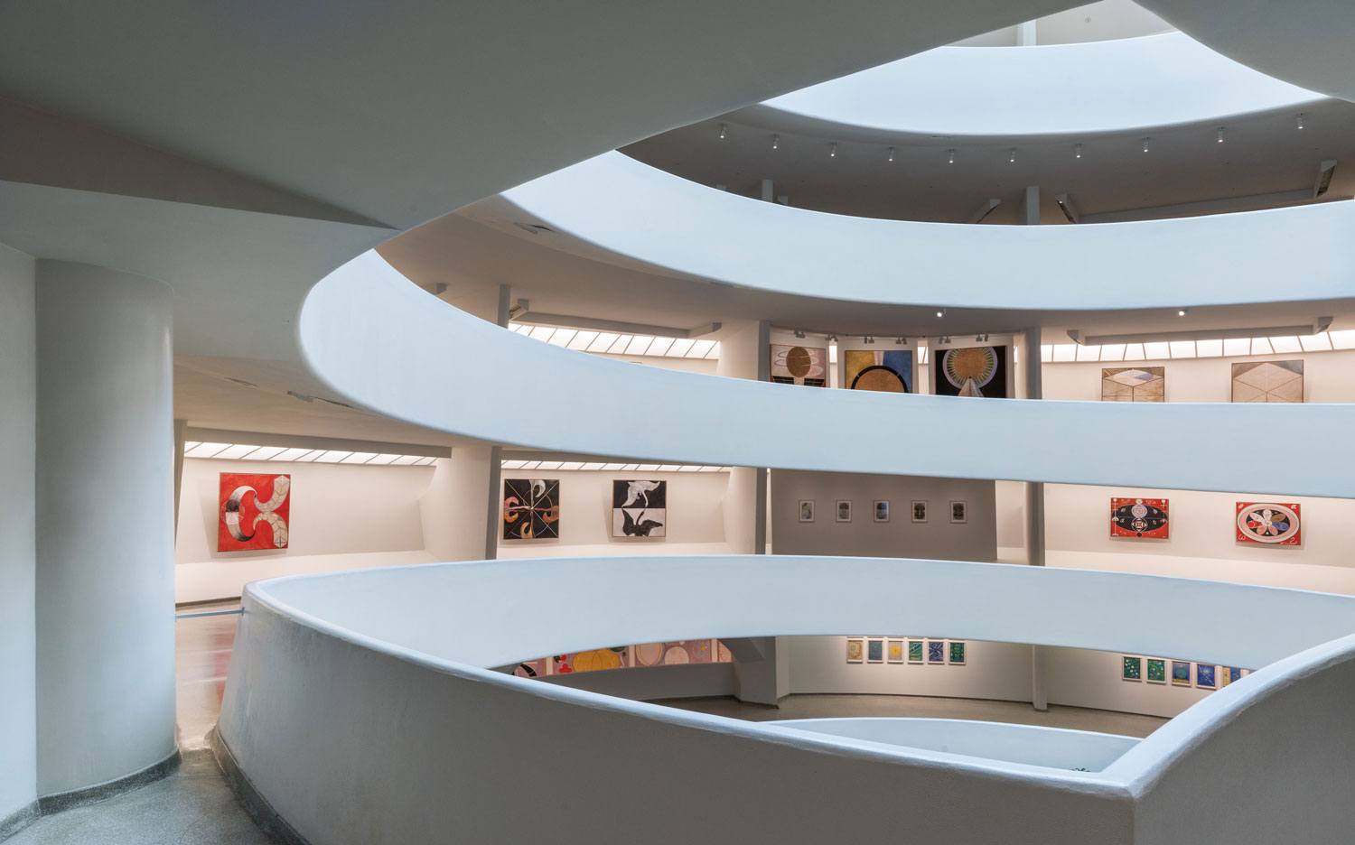 Spiral interior of a modern gallery with art displays on white walls and natural light from overhead openings.