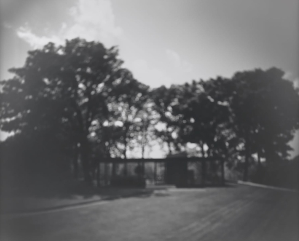 Blurry black and white image of a structure surrounded by tall trees under a cloudy sky.