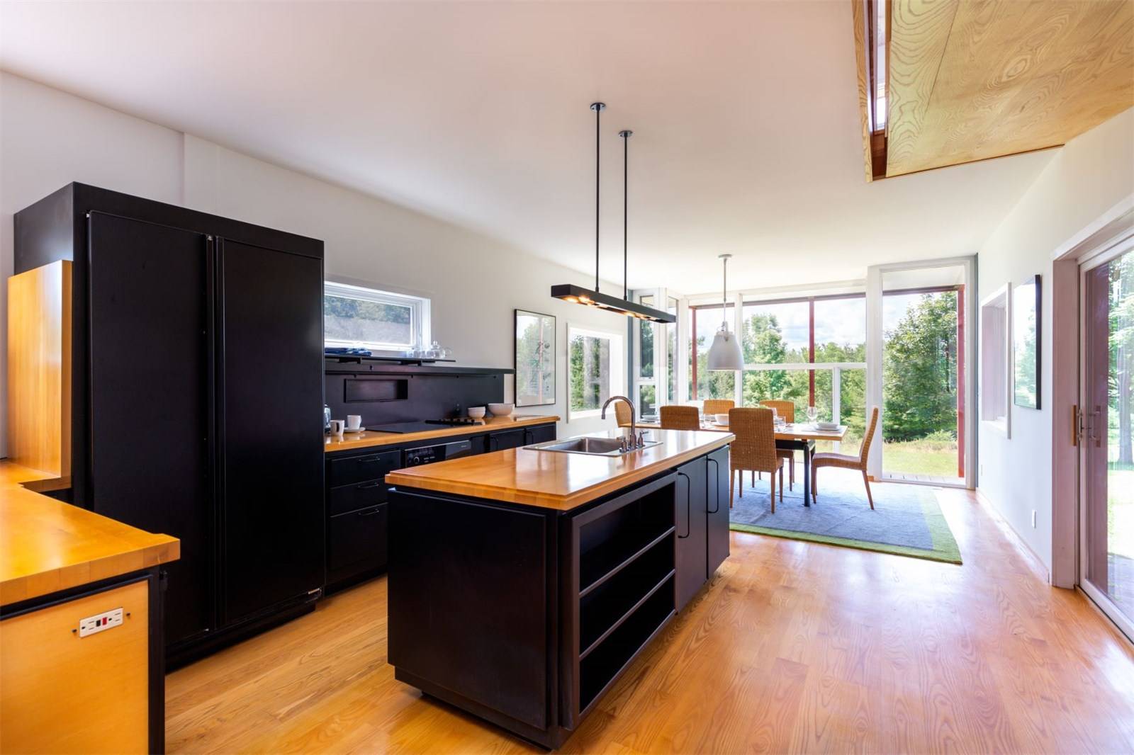 Modern kitchen with black appliances, wooden island, and dining area with large windows overlooking greenery.