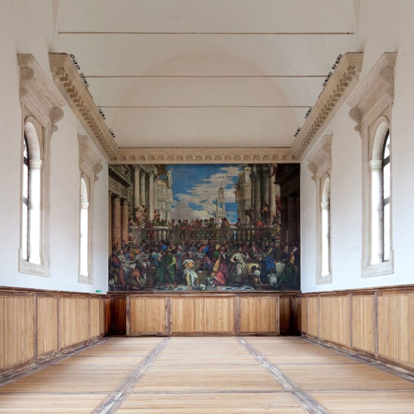 Interior of a large, empty hall with wooden paneling and a detailed mural of a gathering on the far wall.