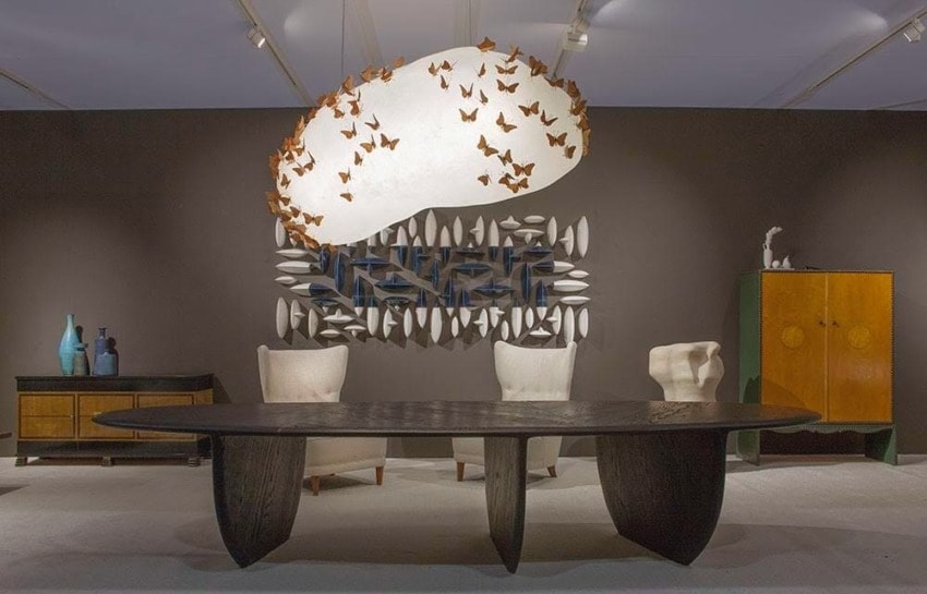 Modern dining room with sculptural table, unique cloud-shaped chandelier, abstract wall art, and elegant chairs.