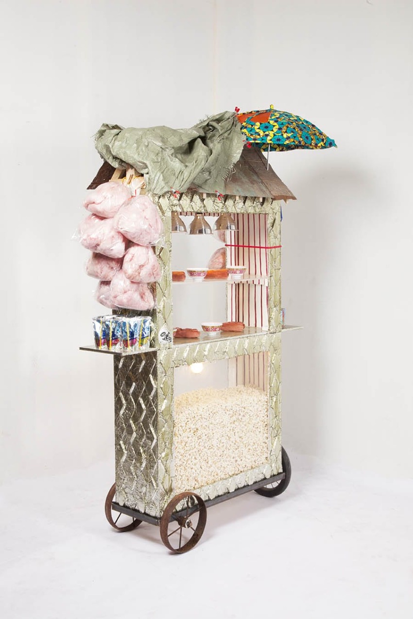 Colorful street food cart with popcorn, hanging pink cotton candy bags, overhanging green cloth, and a vibrant umbrella.