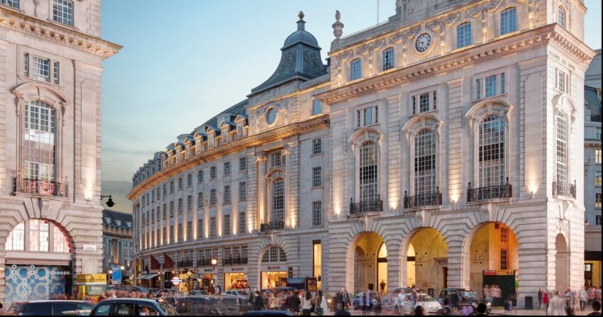 Bustling city street with historic buildings, arched entrances, and a crowd of people at dusk.