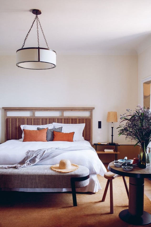 Cozy bedroom with a king-sized bed, decorative pillows, a bench, a side table with flowers, and a large ceiling light fixture.