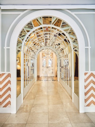 Elegant arched hallway with mirrored panels and intricate ceiling details leading to a well-lit entrance with artwork.