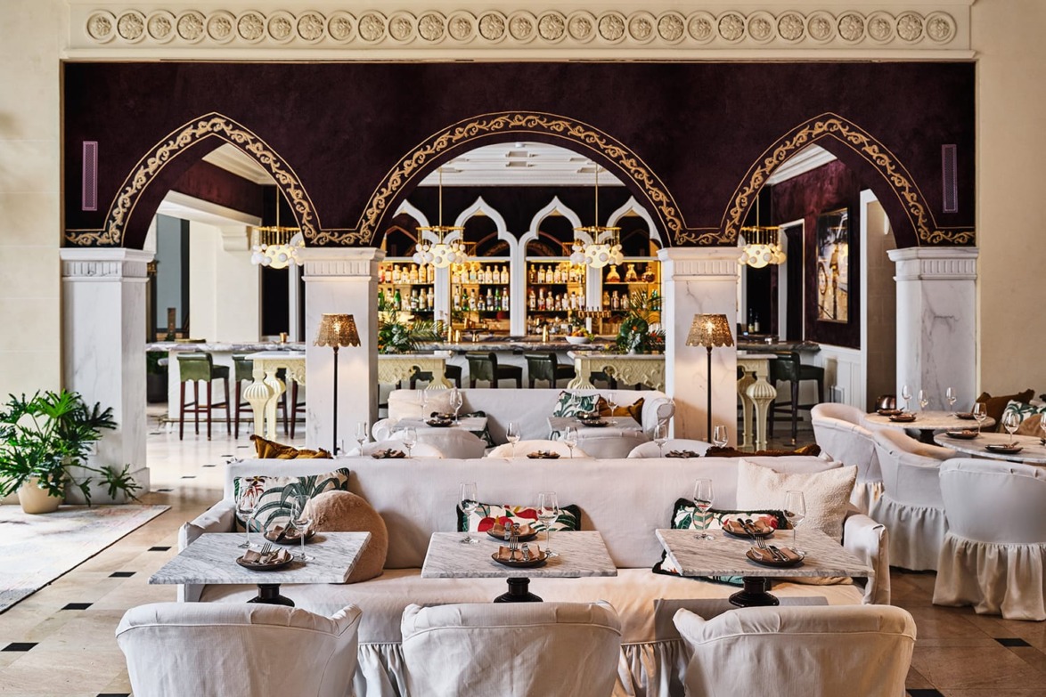 Elegant restaurant interior with white sofas, decorative arches, and a well-lit bar in the background.