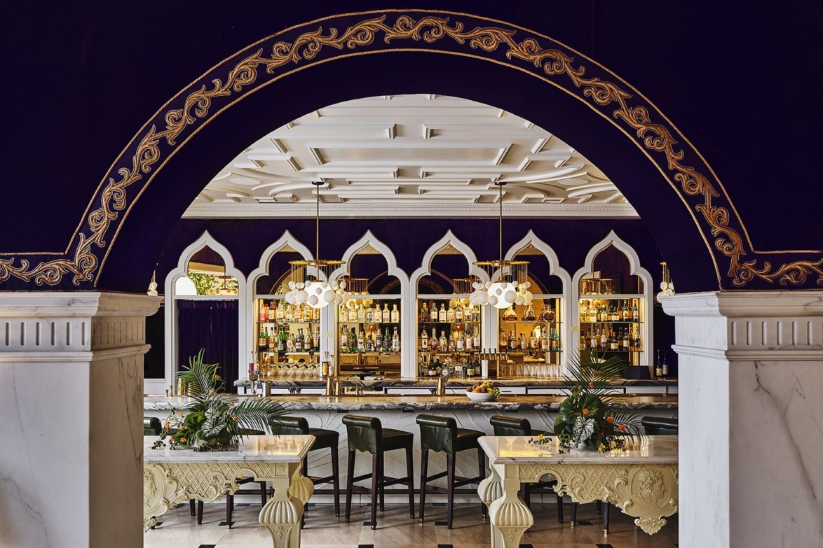 Elegant bar with ornate archway, rows of spirits, and stylish seating, featuring golden accents and ambient lighting.