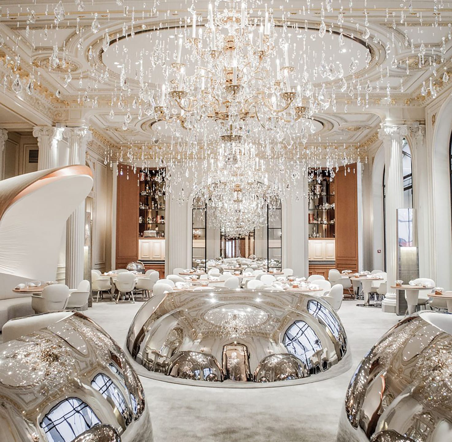 Luxurious dining room with grand chandeliers, elegant white decor, and reflective silver spheres creating a sophisticated ambiance.