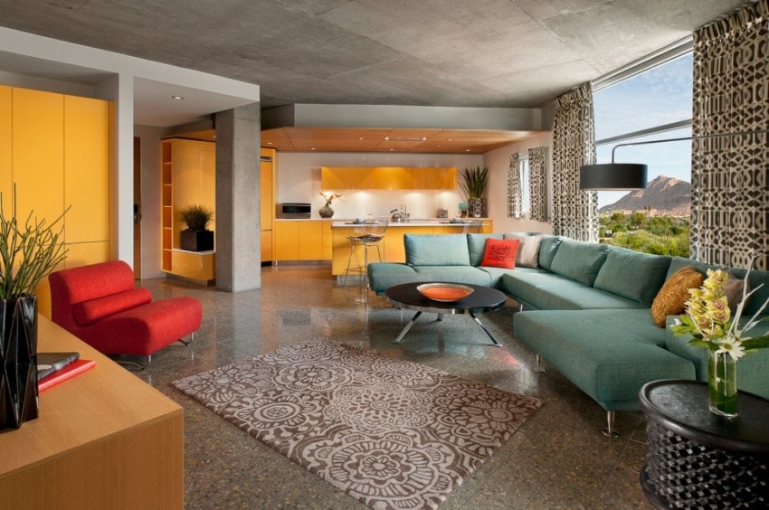 Modern living room with vibrant orange and teal decor, mid-century furniture, and large windows featuring a scenic view.