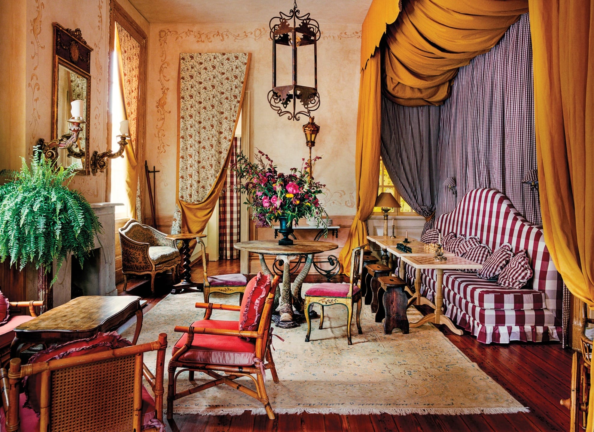 Eclectic vintage living room with striped sofa, floral arrangements, antique chairs, and mustard drapes.