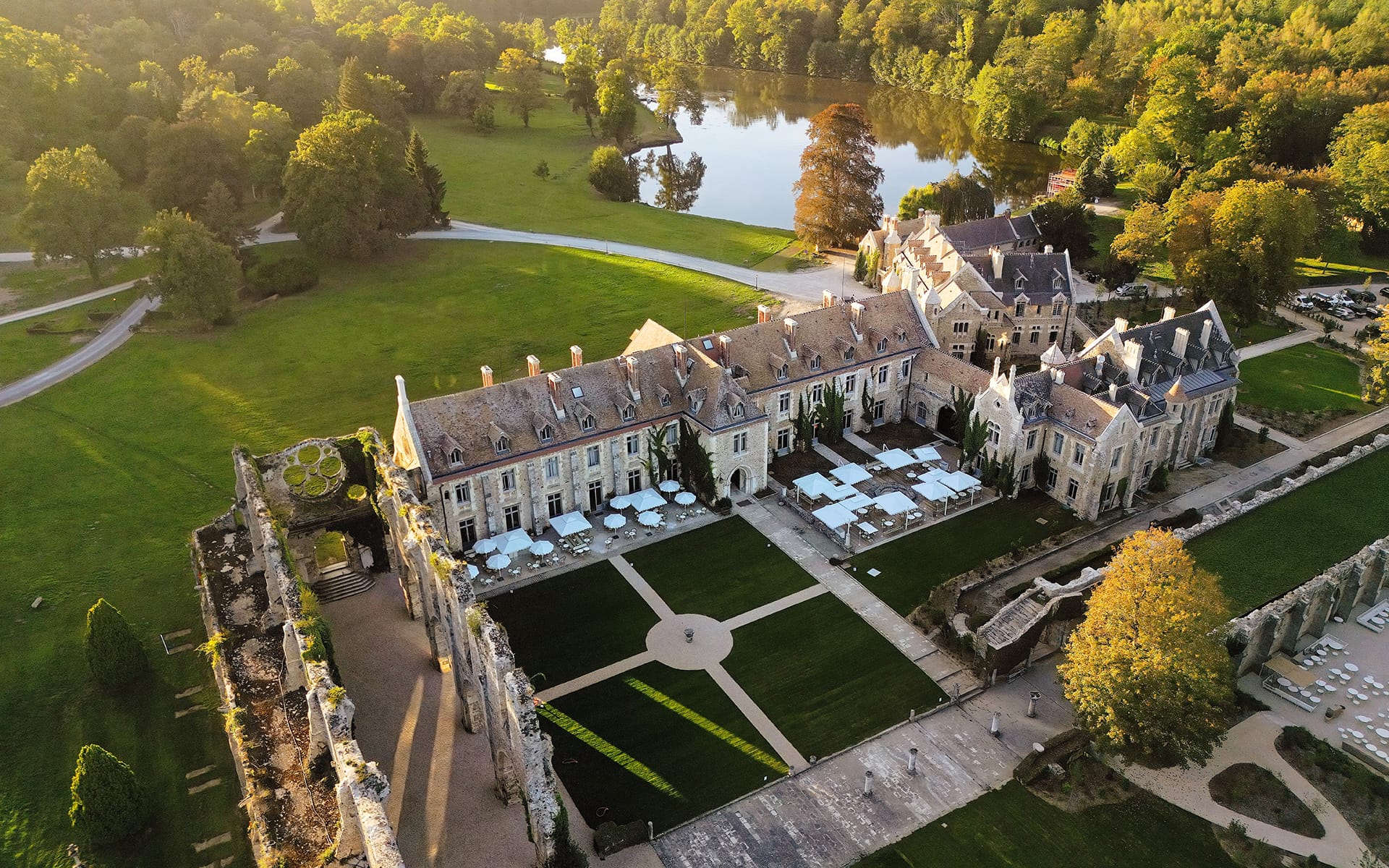 Aerial view of a historic chateau surrounded by lush green gardens and a river in the background.