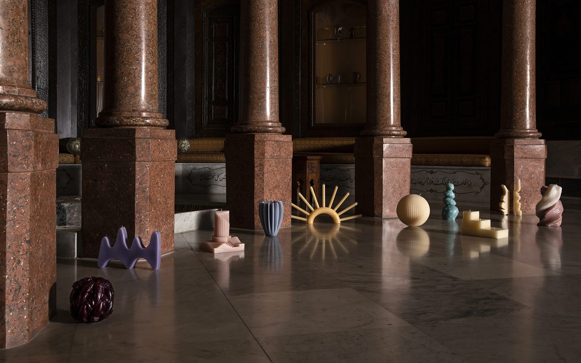 Abstract sculptures displayed on a marble floor in a dimly lit room with large stone pillars.