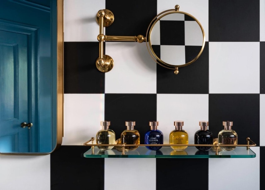 Elegant bathroom with checkered wall, round mirror, and glass shelf holding five colorful perfume bottles.