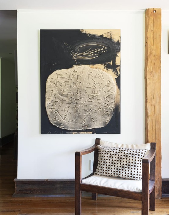 Abstract black and white artwork of a textured sphere on a wall with a wooden chair in front